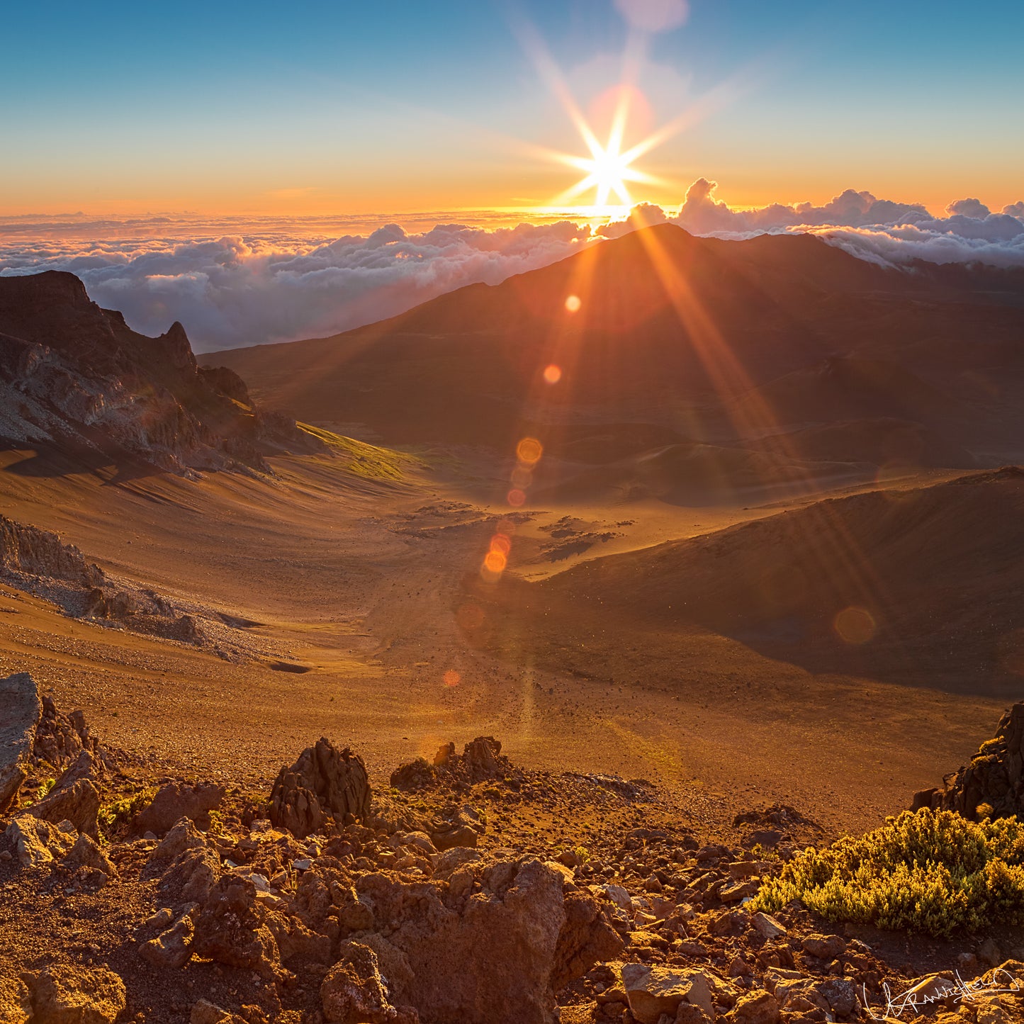 Sunrise over a mountainous landscape with rocky terrain and clouds below.