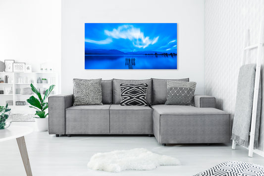 Gray sectional sofa with decorative pillows in a living room setting, featuring a large photograph with a blue sky and water scene.