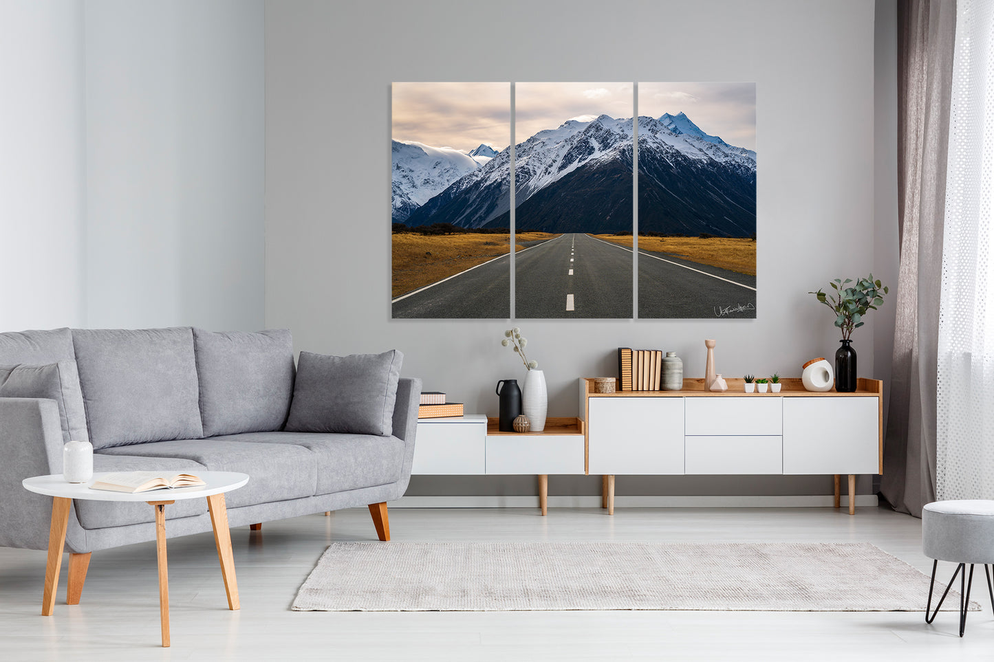 Living room with a gray sofa, coffee table, and a large art triptych of a mountain road.