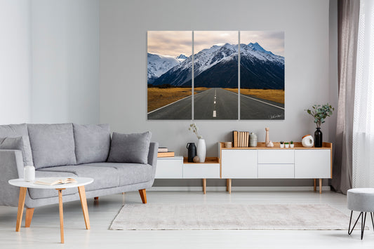 Living room with a gray sofa, coffee table, and a large art triptych of a mountain road.