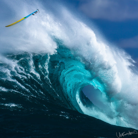 Towering wave with a surfboard caught in its curl, set against a blue sky.