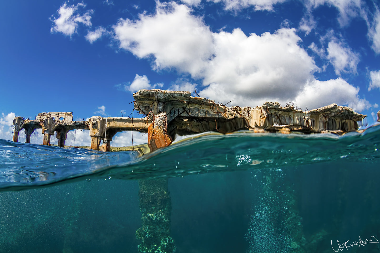 Underwater view of a sunken shipwreck with clear blue water and a partly cloudy sky.