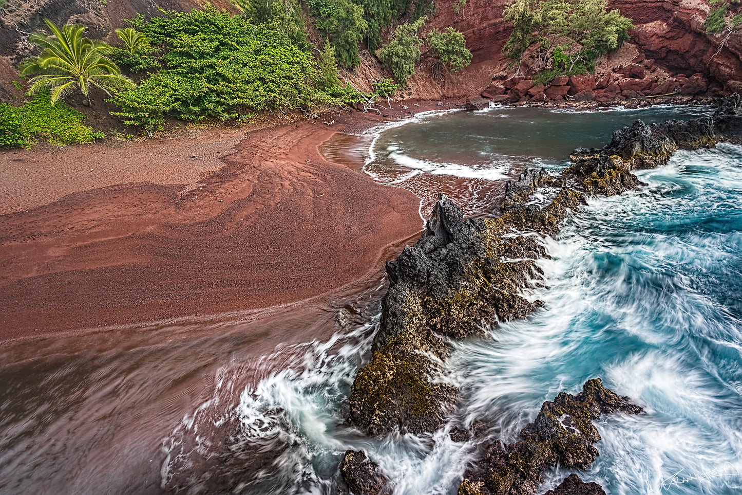 Red sand beach with ocean waves crashing against rocks