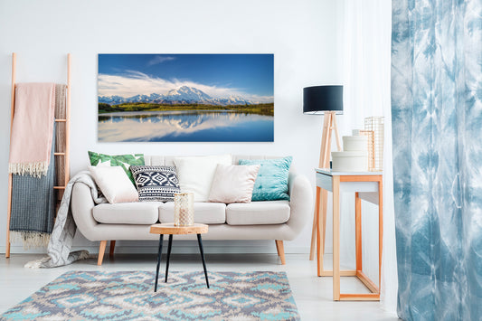 Living room with a large photograph on the wall displaying a mountain landscape, white sofa with decorative pillows, and a rug.