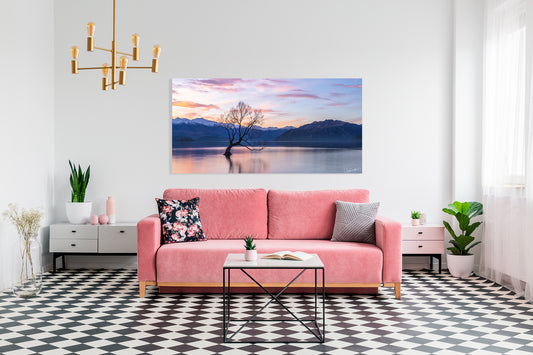 Living room with a pink sofa, coffee table, and wall art of a tree in a lake.