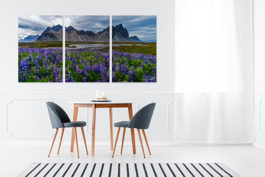 Three-panel wall art of a mountain landscape with purple flowers in a modern interior setting.