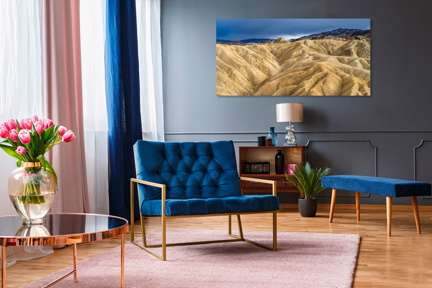Modern living room with blue armchair, coffee table, and wall art of a desert landscape.