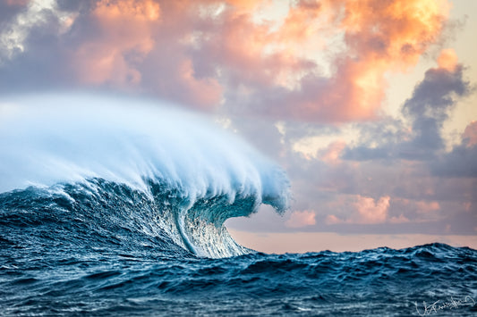 Large wave crashing in the ocean with a colorful sky