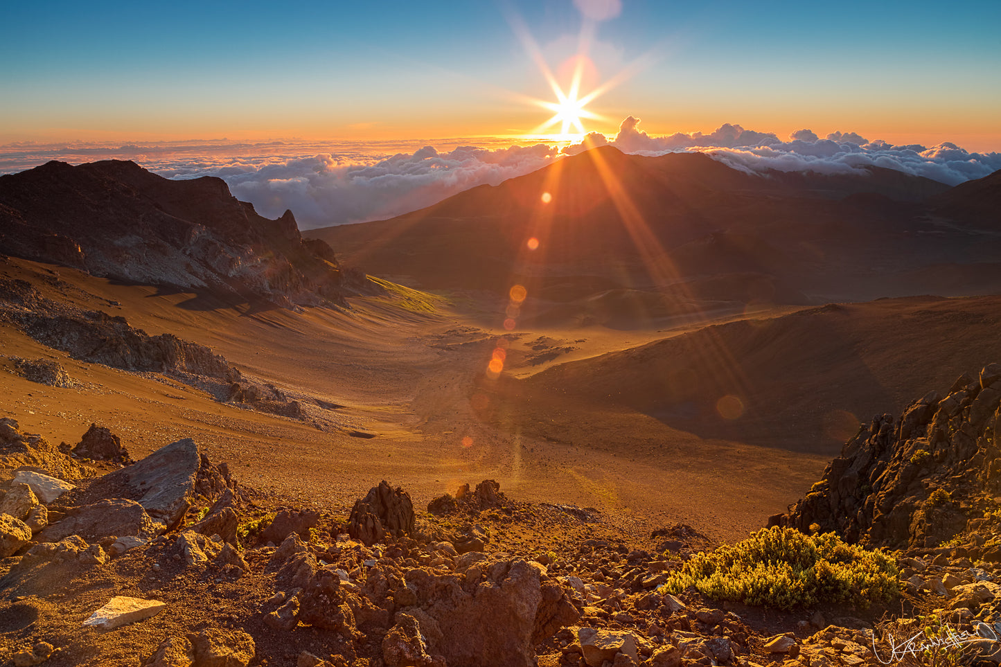 Sunrise over a mountain landscape with rocky terrain and clouds.