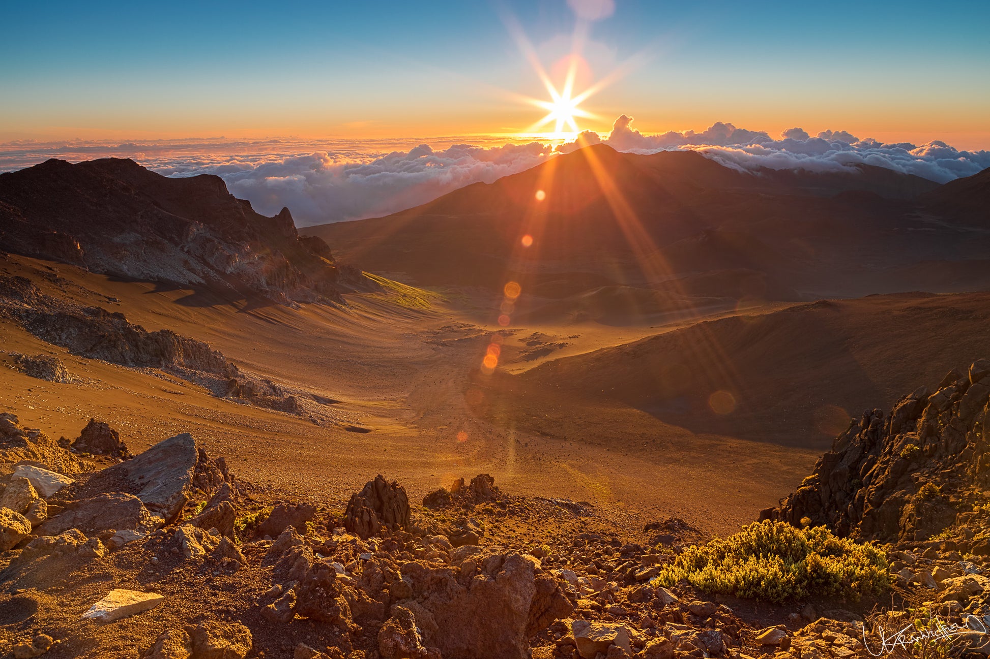 Sunrise over a mountain landscape with rocky terrain and clouds.