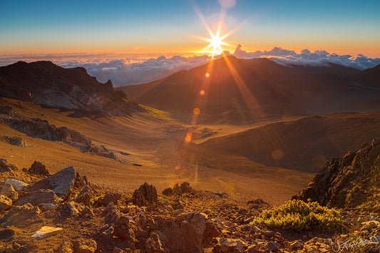 Sunrise over a mountain landscape with rocky terrain and clouds.