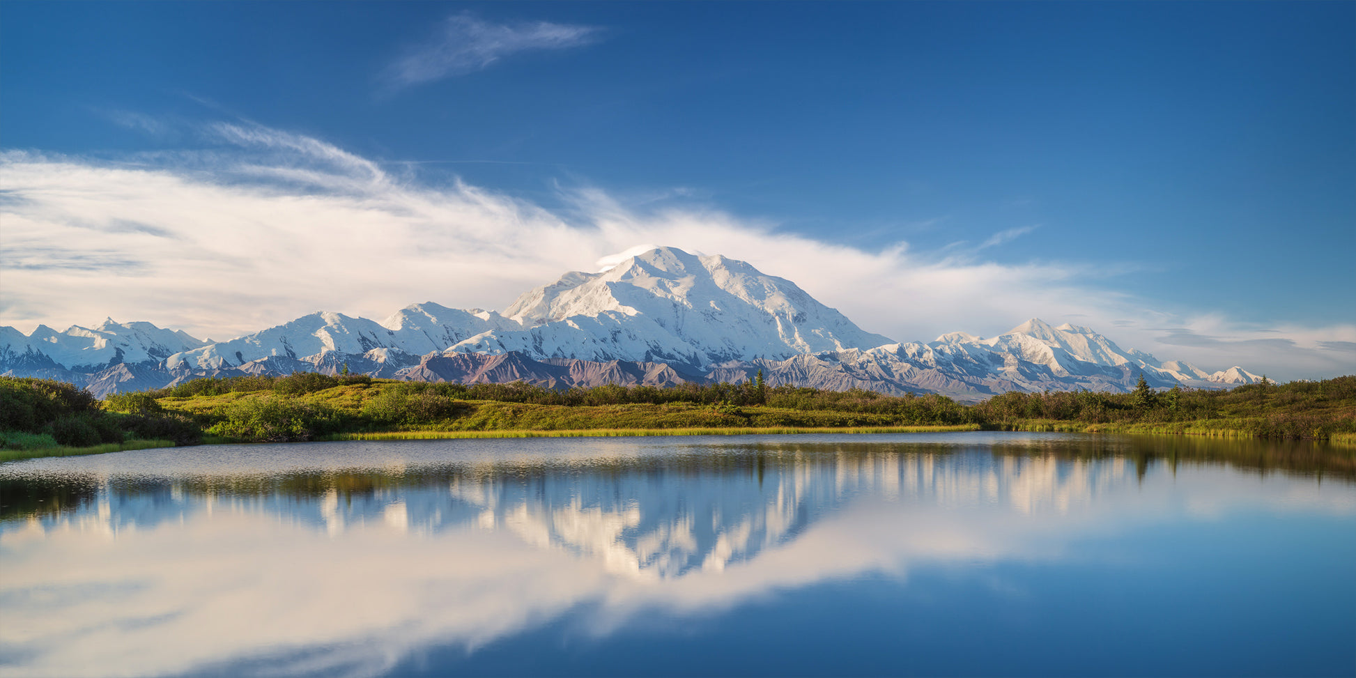 Mountain range reflected in a calm lake with a blue sky.