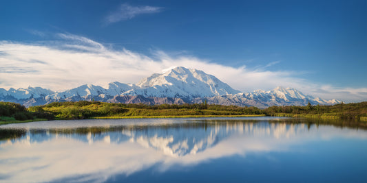 Mountain range reflected in a calm lake with a blue sky.