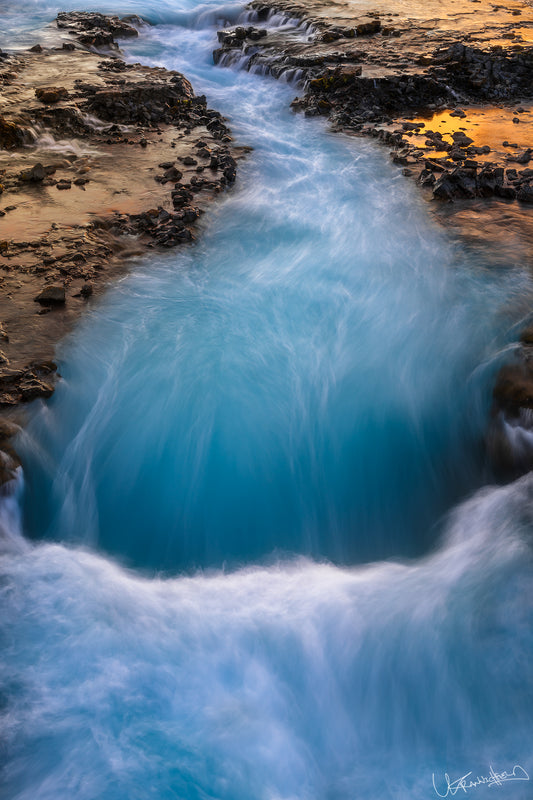 Turquoise water flowing over rocks with a sunset reflection.