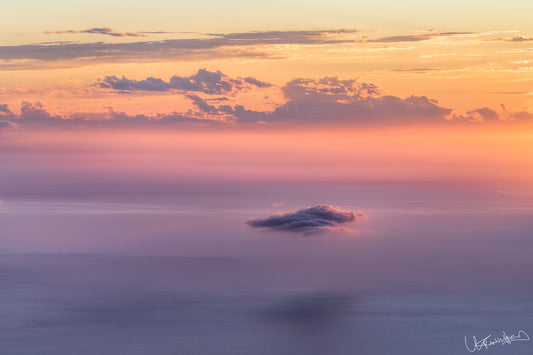 A landscape image featuring a body of water with a cloud formation in the distance, during sunset with a purple hue in the sky.