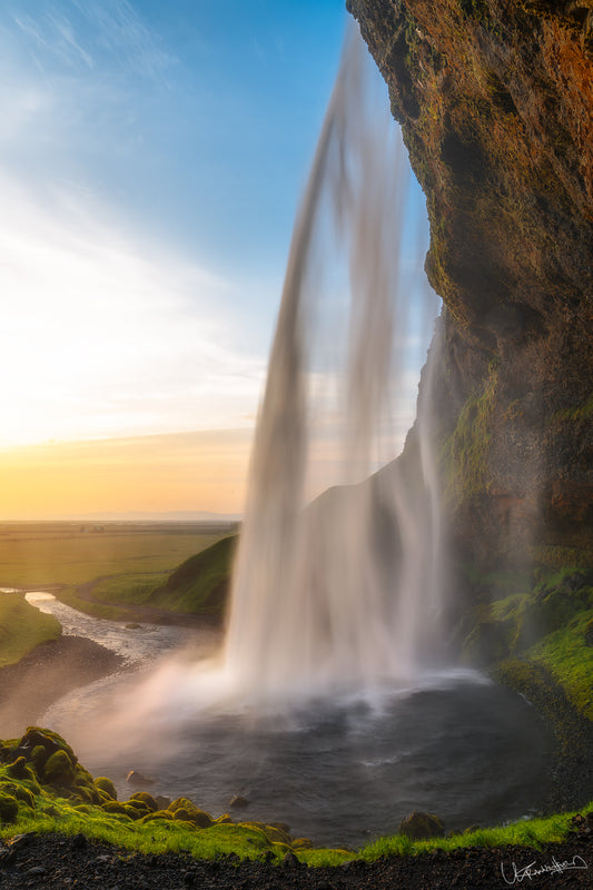 A photograph taken behind a waterfall at sunset