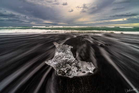 Iceberg on a beach with ocean waves and a dramatic sky