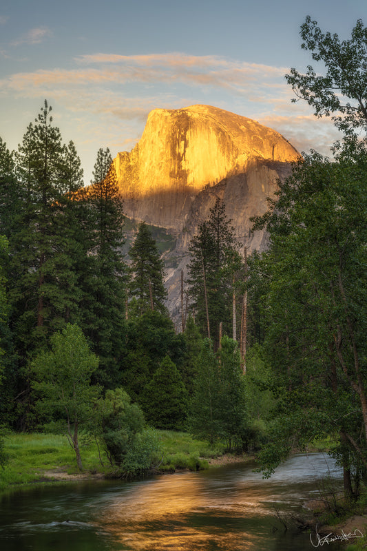 Sunset over Half Dome in Yosemite Valley with trees and a stream in the foreground.