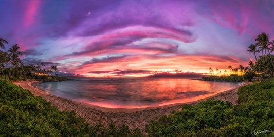 A vibrant image showcasing a beautiful sunset over Kapalua Bay with a visible setting moon and colorful sky reflecting off the water.