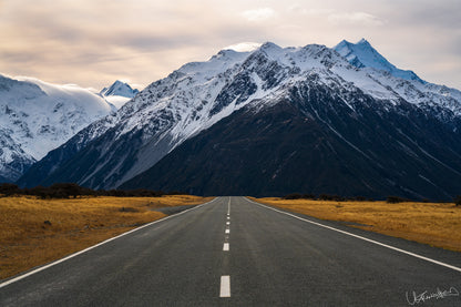 Long road leading to snow-capped mountains under a cloudy sky