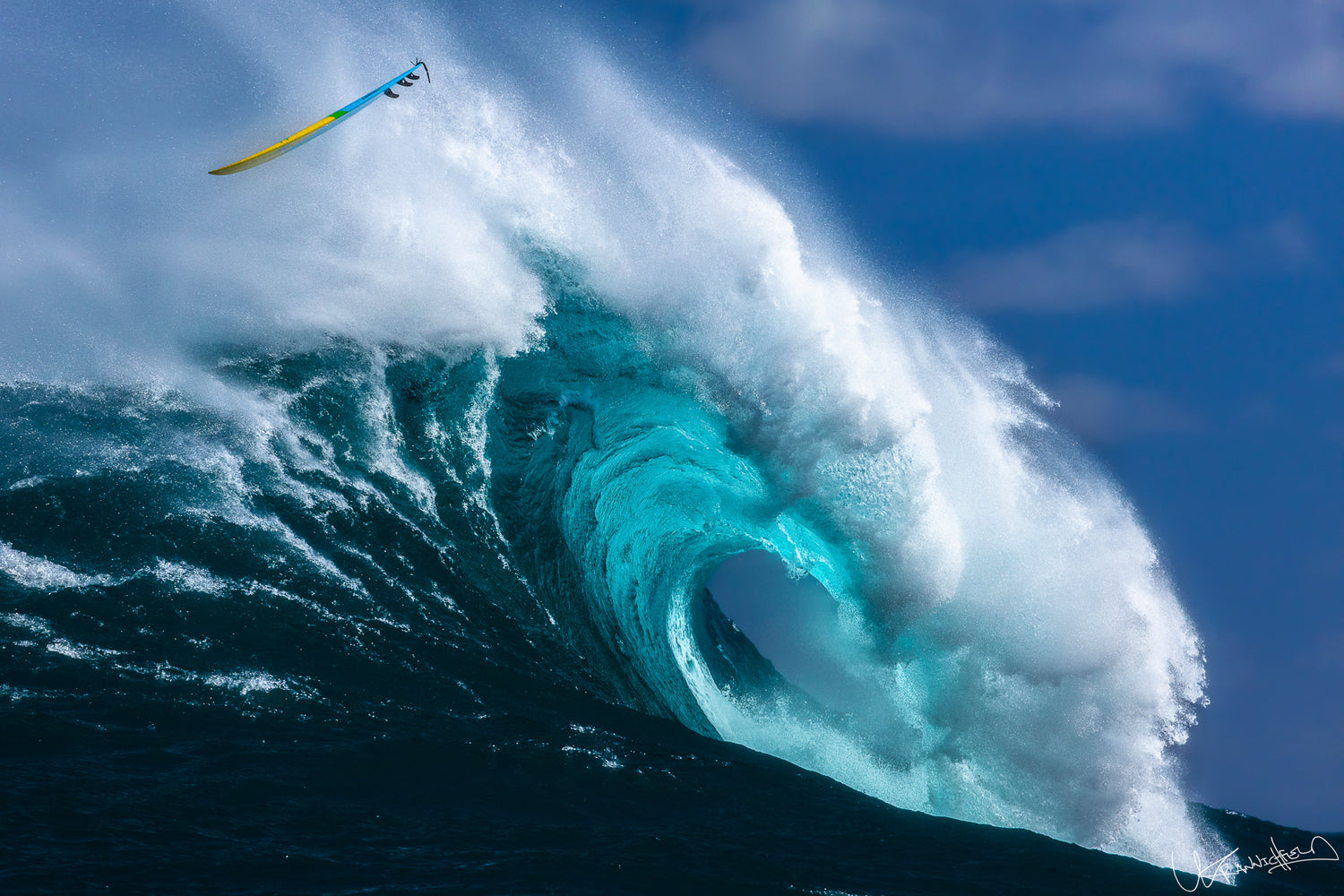 Surfer on a yellow surfboard riding a large wave with blue sky.