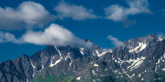 Mountain range with snow-capped peaks under a blue sky with clouds