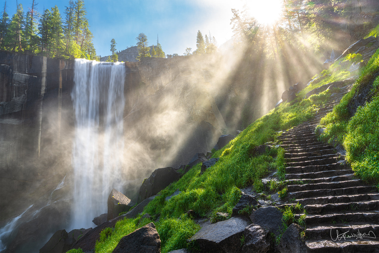 Waterfall with sunlight beams and steps leading up a green hillside