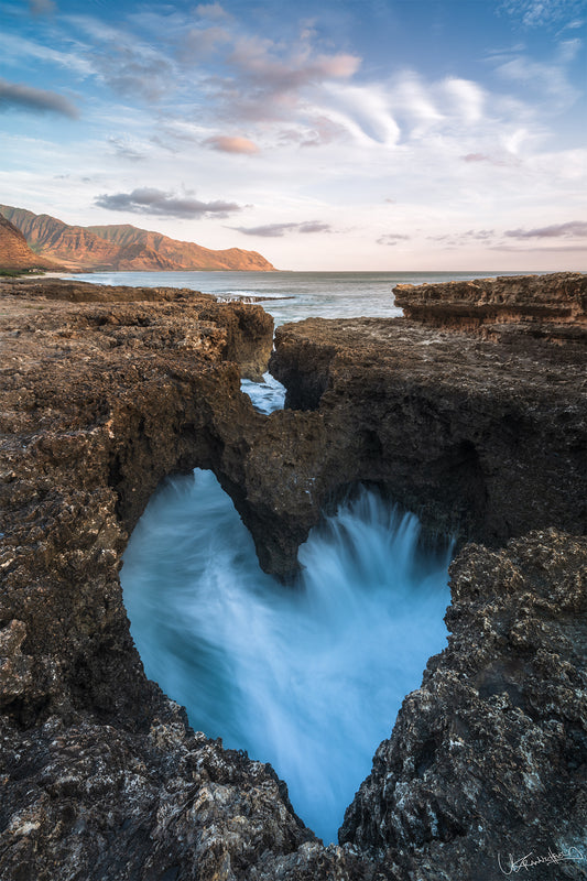 A natural heart-shaped formation in rocks by the coastline with water flowing through it, capturing the essence of Hawaii.