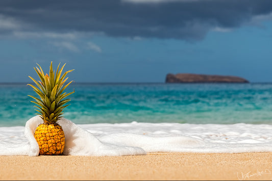 Pineapple on a sandy beach with ocean and island in the background