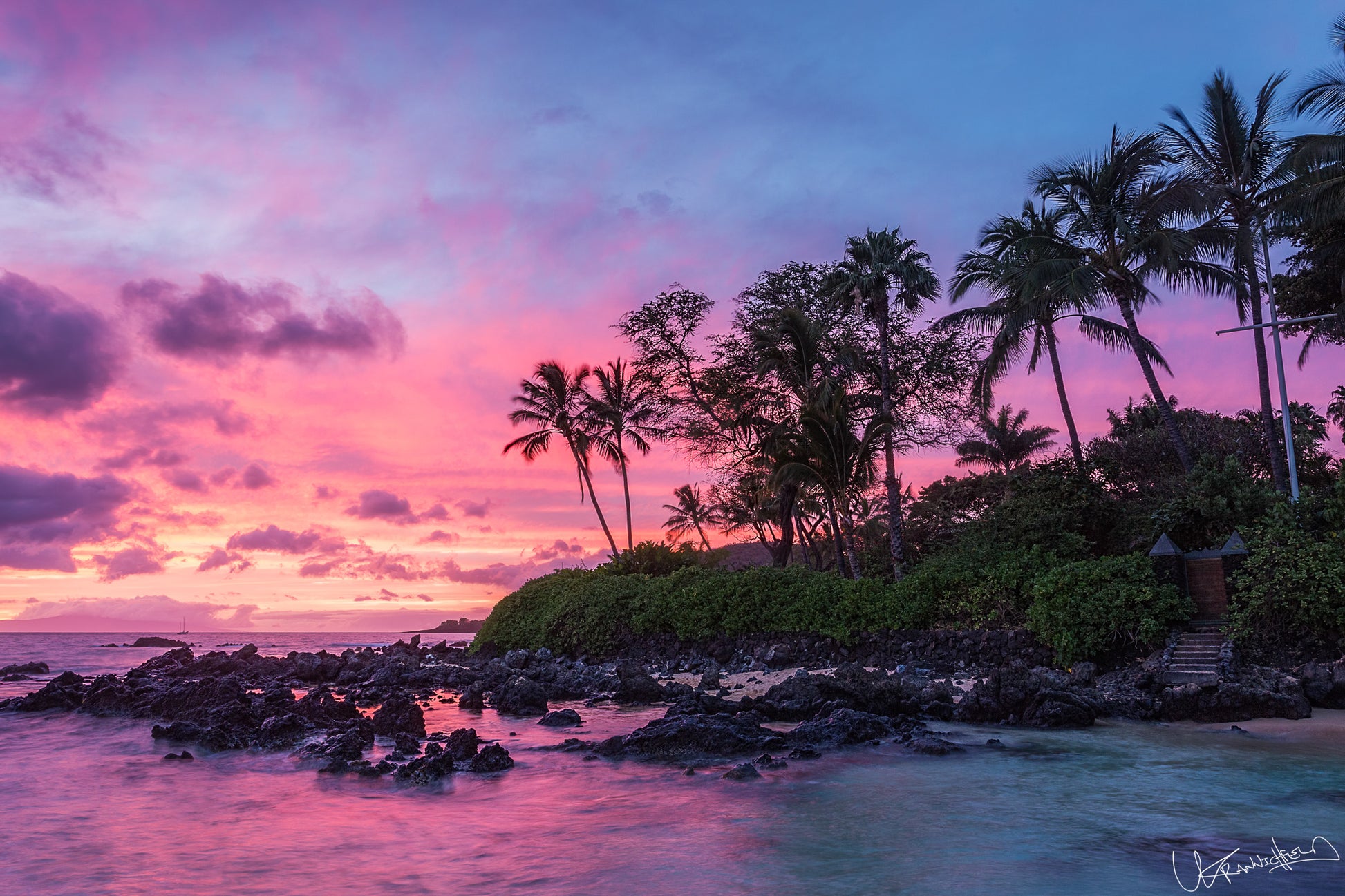 Sunset over a tropical island with palm trees and rocky shore.