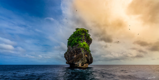 Island rock formation in the middle of the ocean with a dramatic sky.
