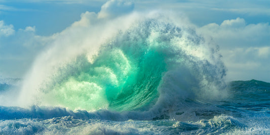 A powerful ocean wave breaking close to the shore, with white foam and blue water, indicating dynamic and energetic sea conditions.